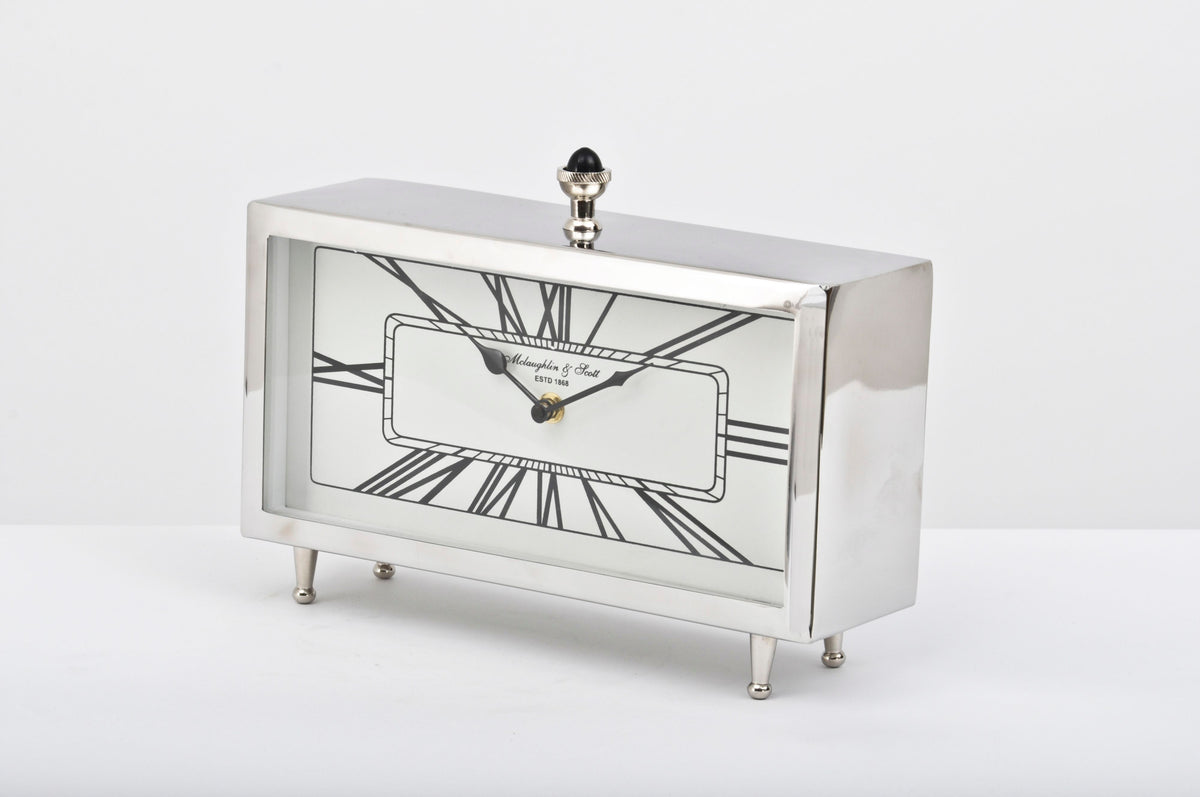 Aeon table clock viewed at an angle, showing its reflective silver case, Roman numeral dial, four small feet and black domed finial.