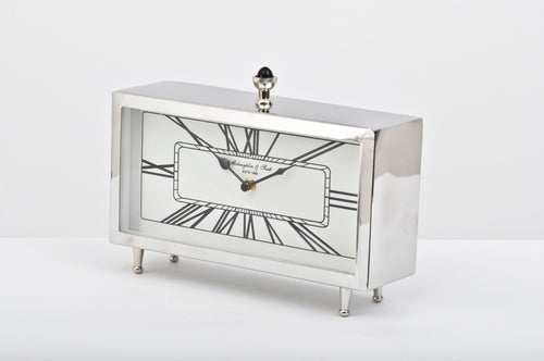 Aeon table clock viewed at an angle, showing its reflective silver case, Roman numeral dial, four small feet and black domed finial.