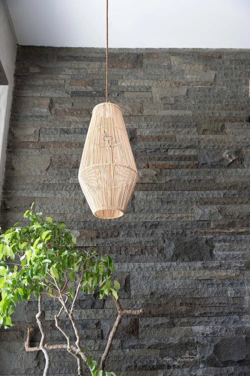 Afrodisiac Rattan Pendant Light – Natural, Medium – suspended against a dark stone wall