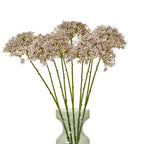 Several lilac-grey botanical sprays arranged in a translucent green vase, with clustered florets spread across the top and the vase partly cropped.