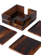 Close view of the patterned coaster holder, showing its brass line, open sides and brown interior, with loose coasters around it.