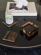 Amber banded coasters and holder on a dark reflective table, with a lemon drink on one coaster and a book behind.