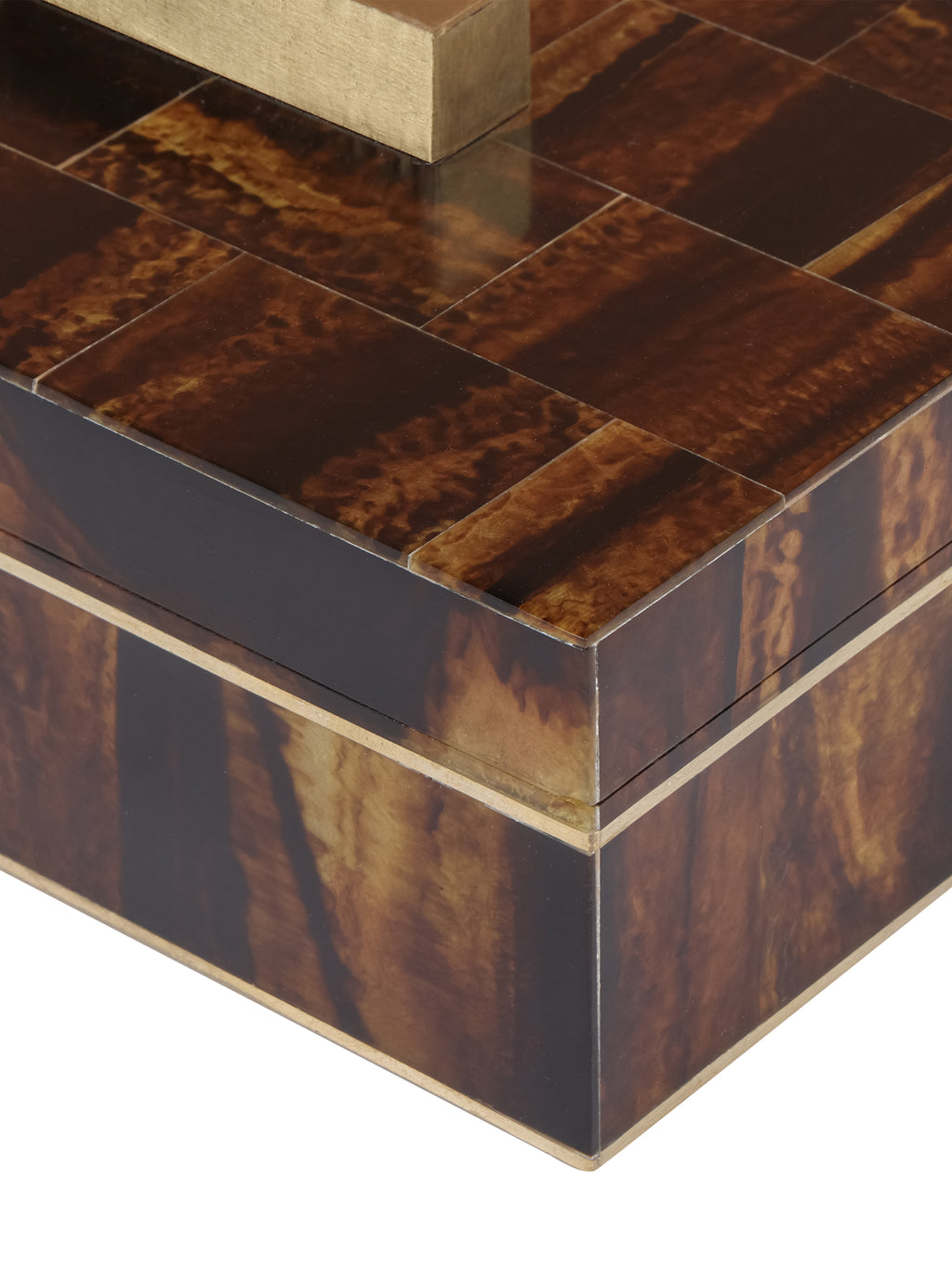 Close-up of the box's glossy amber and brown patterned lid, brass handle and fine brass trim around the corner.