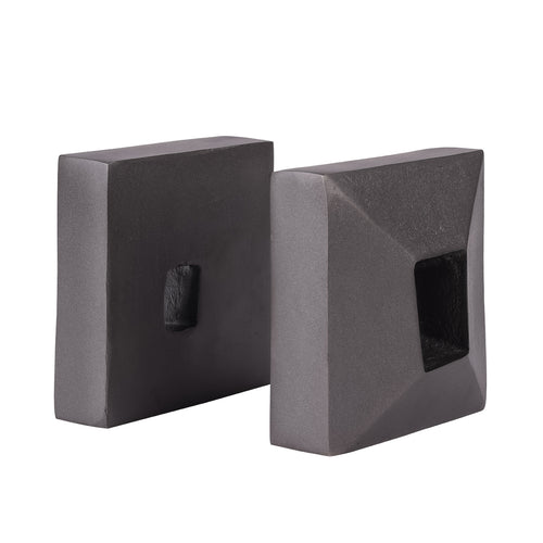 Charcoal grey bookends at an angle, showing one broad rear face with a small opening and one faceted face with a deep recess.