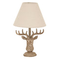 Front view of a stag head table lamp with wide brown antlers, a stepped circular foot and a pale tapered shade on a white background.