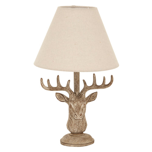 Front view of a stag head table lamp with wide brown antlers, a stepped circular foot and a pale tapered shade on a white background.