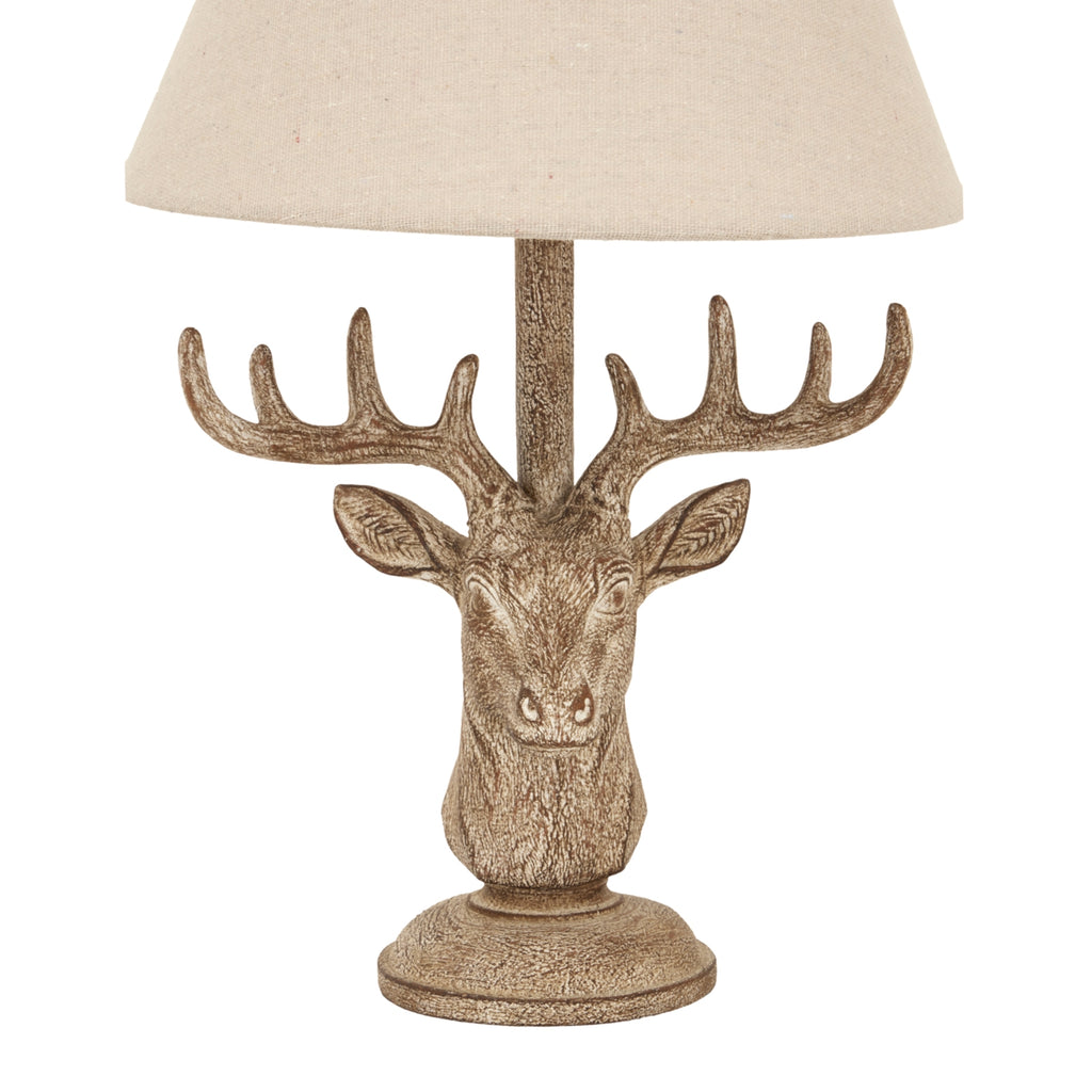 Close-up of the lamp's textured stag face, branching antlers and mottled brown pedestal beneath the lower edge of the woven-looking shade.