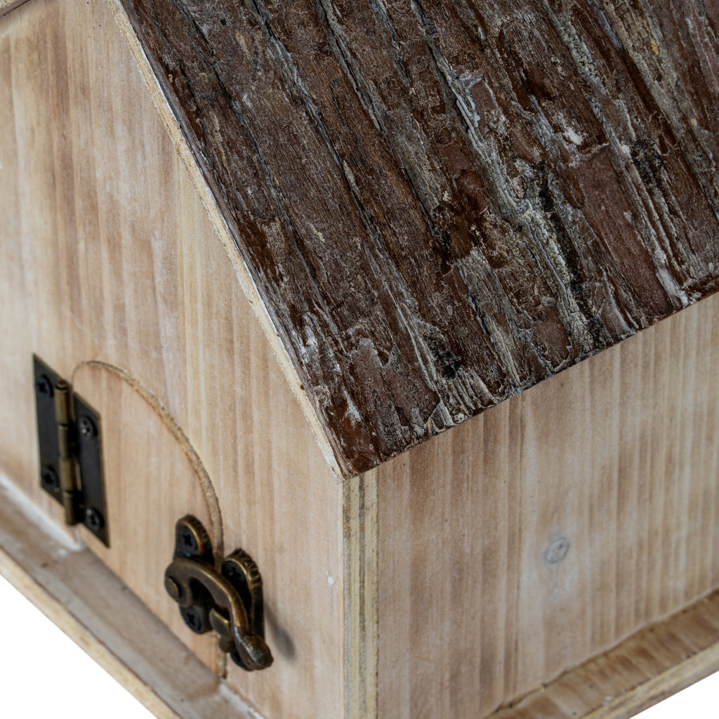 Angled detail of the birdhouse's dark, rough-textured roof above the pale side wall, with part of the arched rear door and latch visible.