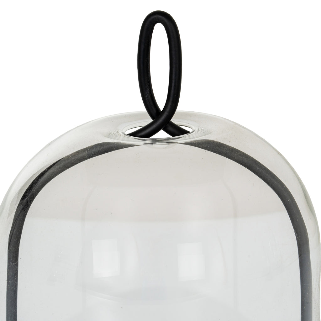 Close-up of the black oval loop passing through the circular opening at the top of the clear cloche, with the curved frame visible below.