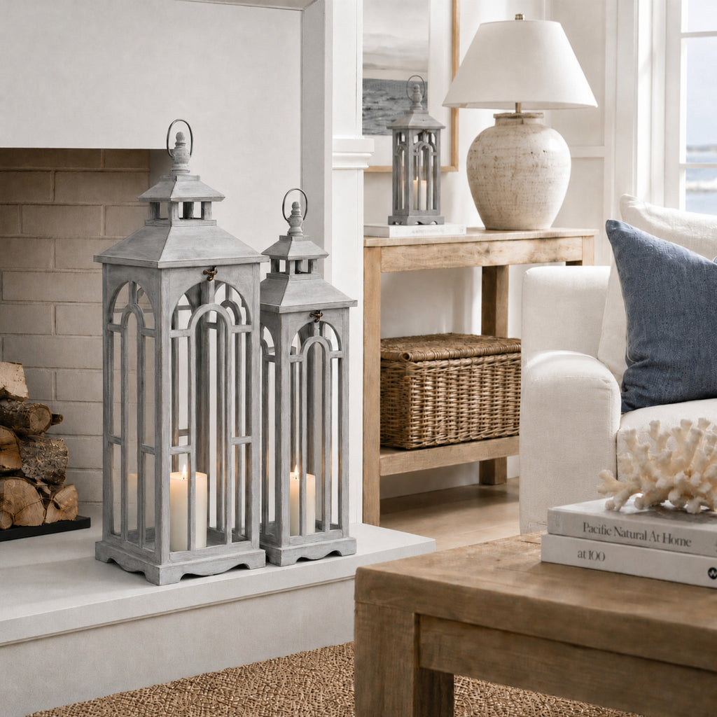 Two grey arched lanterns on a white hearth, with a third on a wooden side table beside a cream lamp.