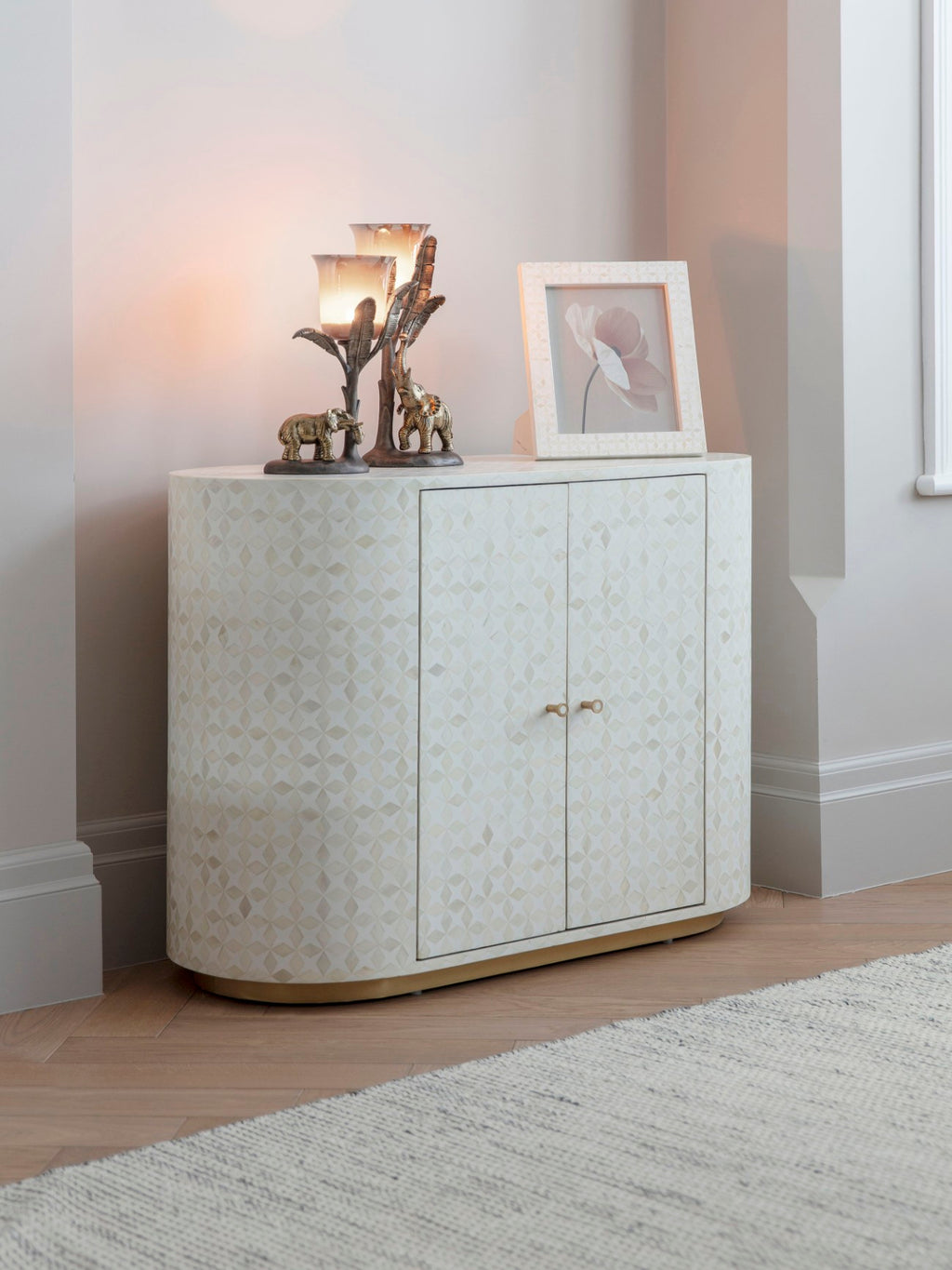 White bone-inlay photo frame holding a flower image on a patterned cabinet beside two lit decorative candleholders with elephant figures.