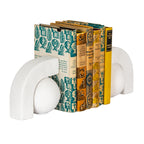 Off-white ball-and-arch bookends flanking a row of books with patterned cream, teal and yellow covers, viewed at an angle.