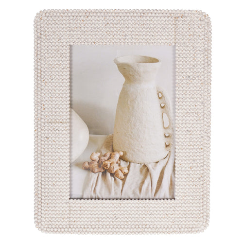 Straight-on view of the cream frame with a broad beaded border surrounding a photograph of pale pottery and draped fabric.