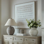 Beige Lineblocks Framed Artwork above a pale sideboard, styled with a ribbed lamp, stacked books and a large vase of green foliage and white flowers.