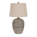 Table lamp on a white background with a rounded black and cream striped body, tapered beige shade, gold-coloured neck and round finial.
