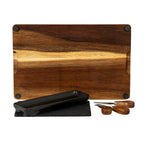 Underside of the brown grained board showing four black corner pads, with the black dish, dark insert and three utensils positioned in front.