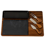 Overhead view of the cheese board arrangement, with the black dish above the dark insert and a two-prong fork and two knives along the right side.