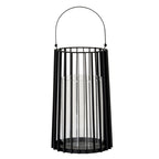 Full view of a tall black lantern with an upright arched handle, vertical rods, broad outer fins and a clear cylindrical inner holder.