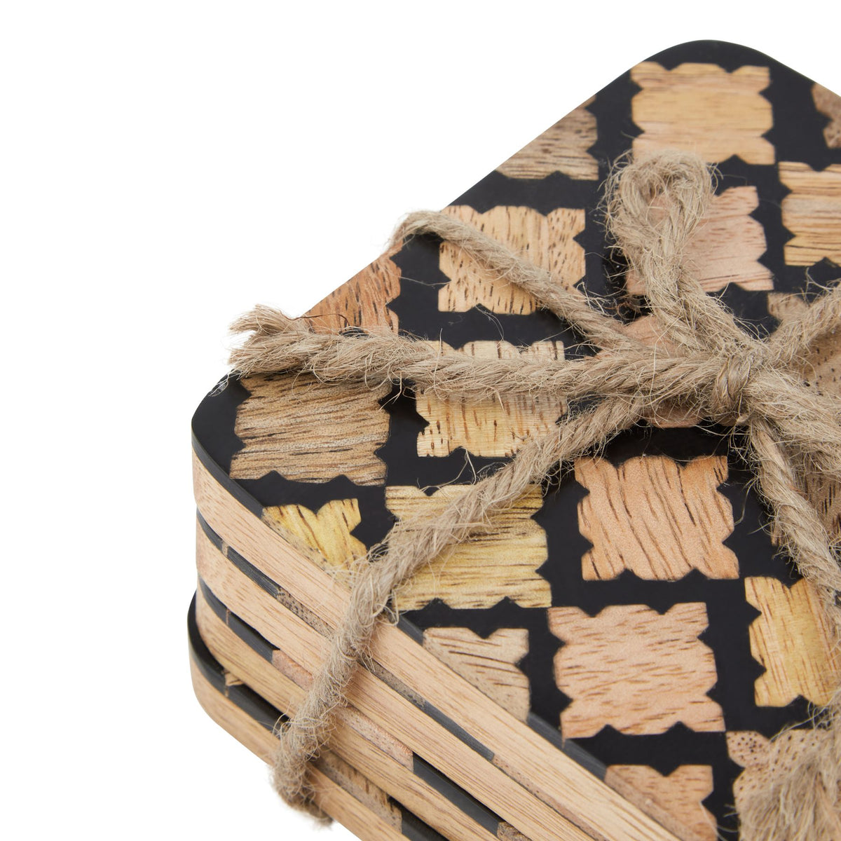 Close-up of the coaster stack showing grained tan quatrefoil-like motifs against black, a rounded corner and the twine bow.