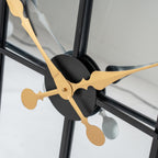 Close-up of the shaped gold-coloured clock hands over the black circular centre, with their reflections visible in the mirrored face.