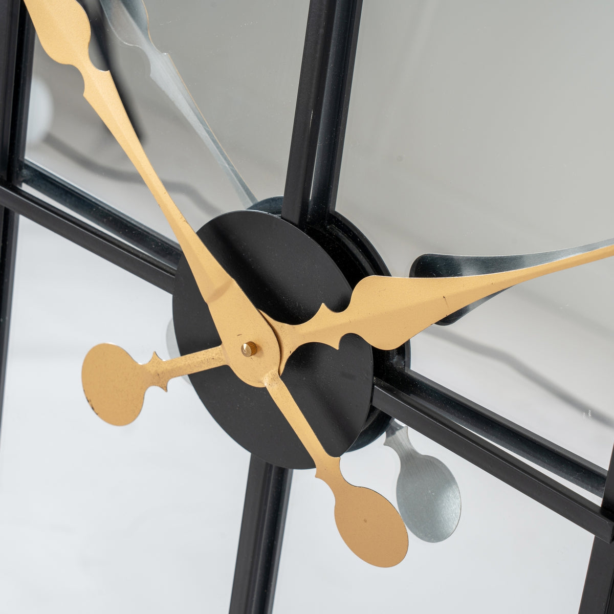 Close-up of the shaped gold-coloured clock hands over the black circular centre, with their reflections visible in the mirrored face.