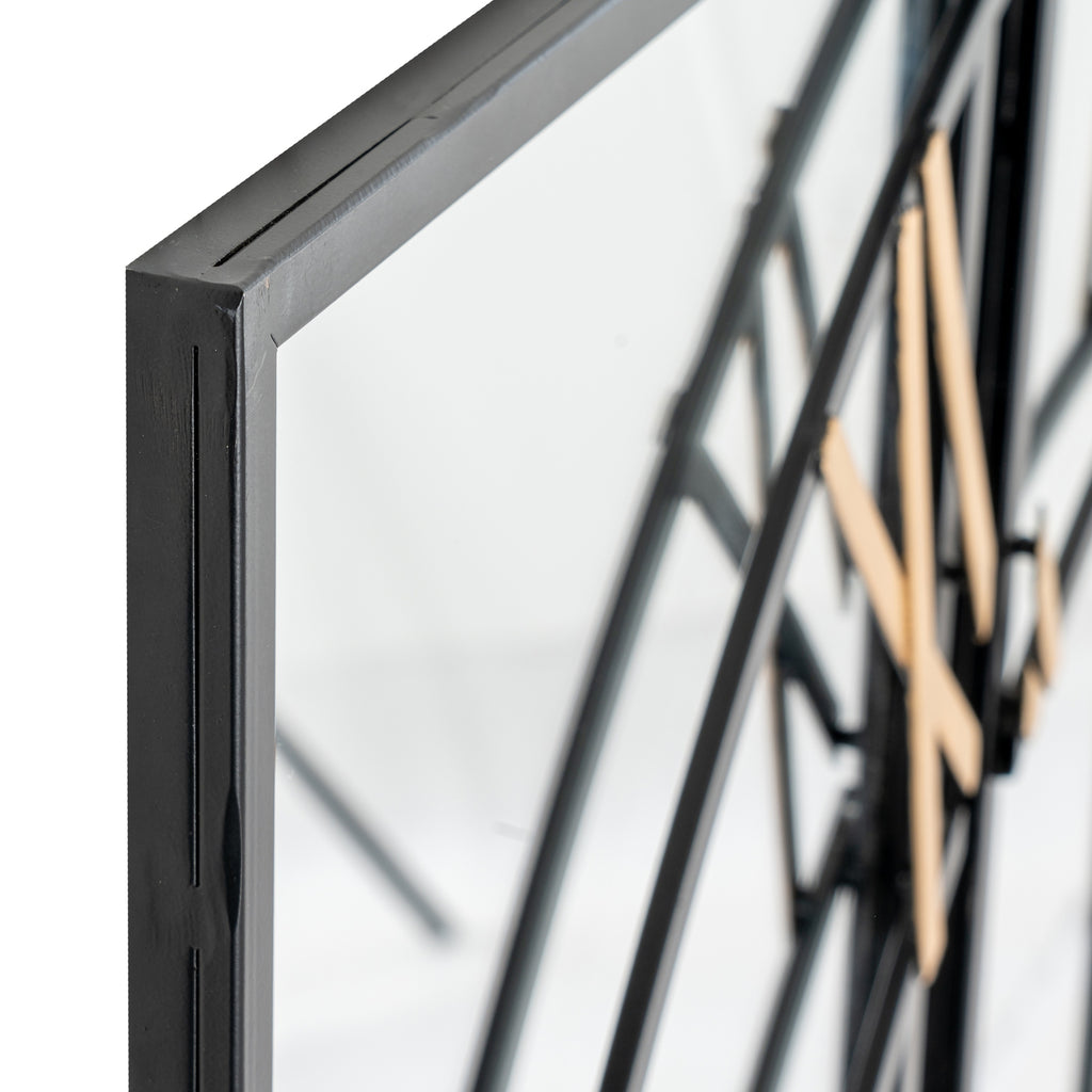 Angled close-up of a black frame corner beside the mirrored clock face, with curved black dial bars and gold-coloured numerals behind.