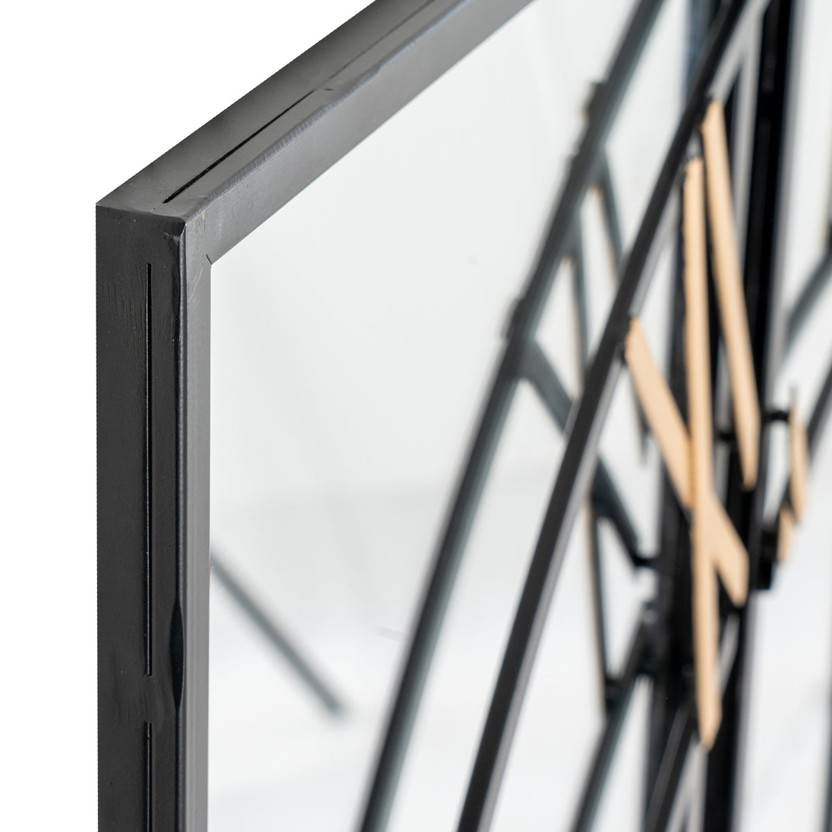 Angled close-up of a black frame corner beside the mirrored clock face, with curved black dial bars and gold-coloured numerals behind.
