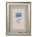 Front view of portrait artwork showing a many-petalled blue flower on a slender grey leafy stem, within a beige woven-looking surround, reflective-looking border and golden-brown frame.