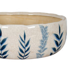 Close-up of dark and pale blue leafy stems on the planter's off-white crackle-patterned surface, with the rounded rim and beige interior above.