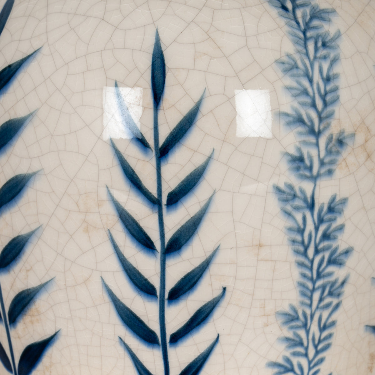 Detail of dark cobalt leaves beside a finer pale blue leafy stem over the vase’s glossy off-white crackle pattern.