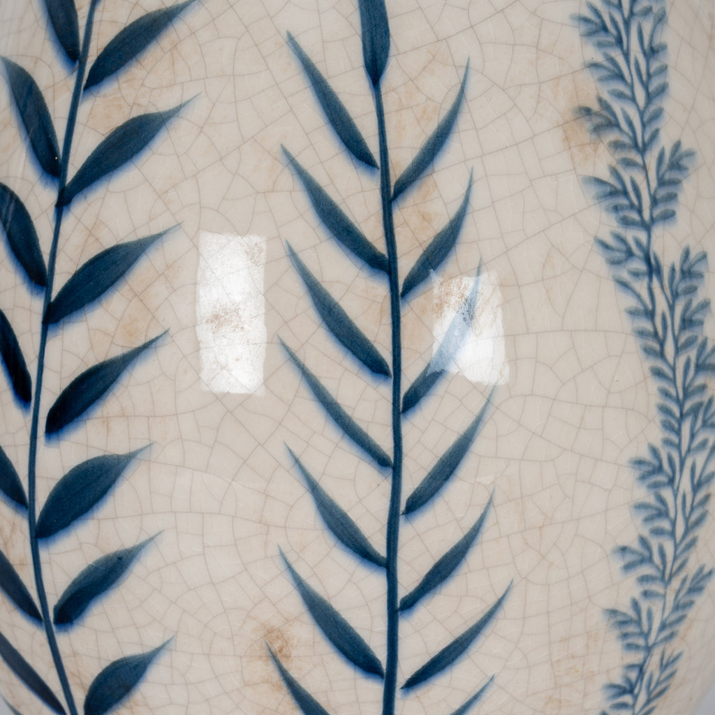 Detail of broad blue leaves and fine blue sprigs against a glossy cream surface with crackle lines and soft brown markings.
