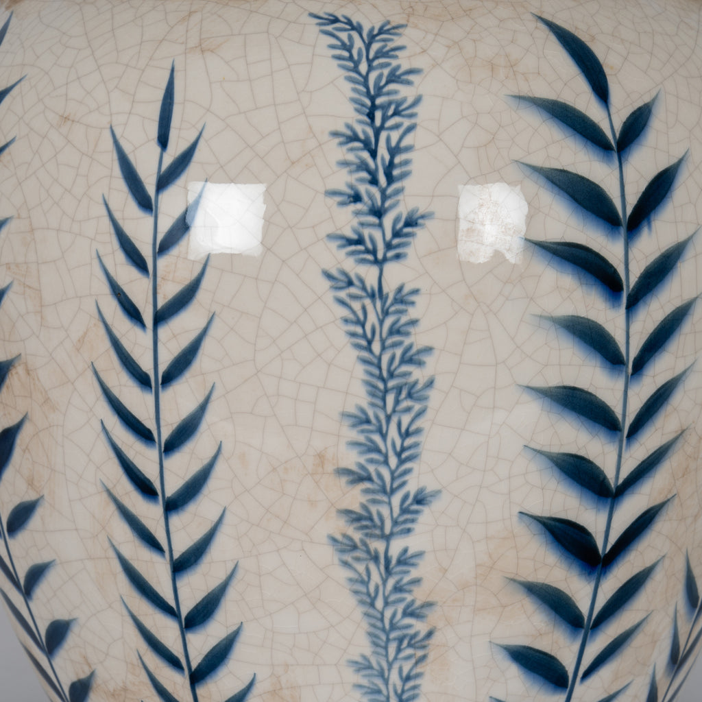 Close-up of alternating dark and pale blue leafy stems over glossy off-white glaze, showing the fine crackle pattern and scattered beige-brown marks.