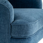 Close-up of the blue armchair's finely textured surface, rounded arm and thick seat cushion edged with matching piping.
