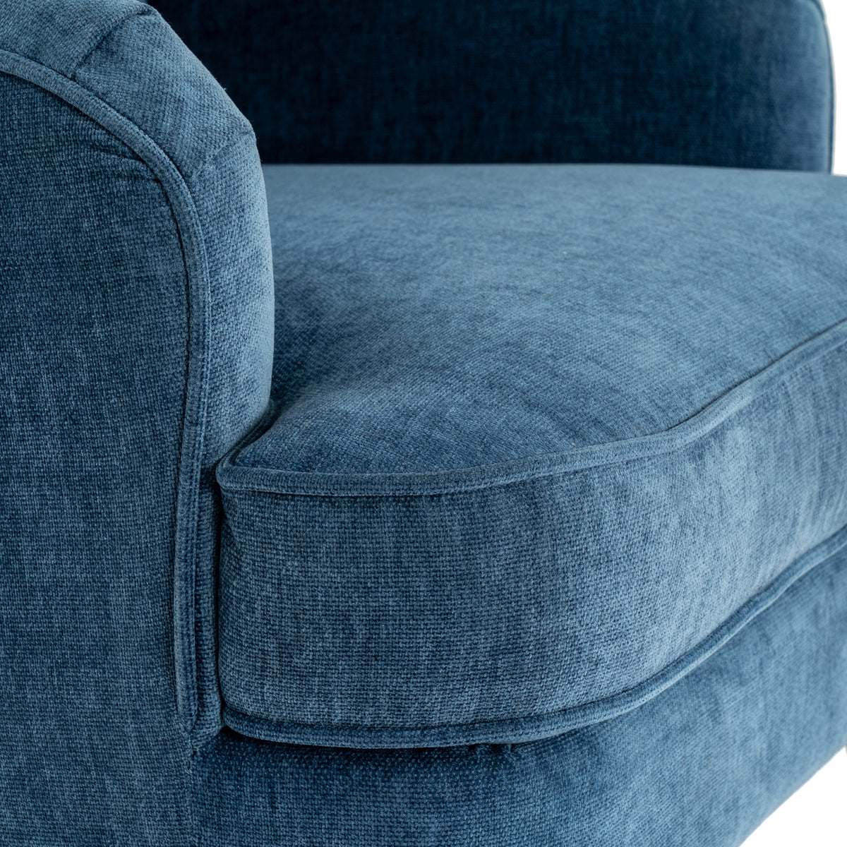 Close-up of the blue armchair's finely textured surface, rounded arm and thick seat cushion edged with matching piping.