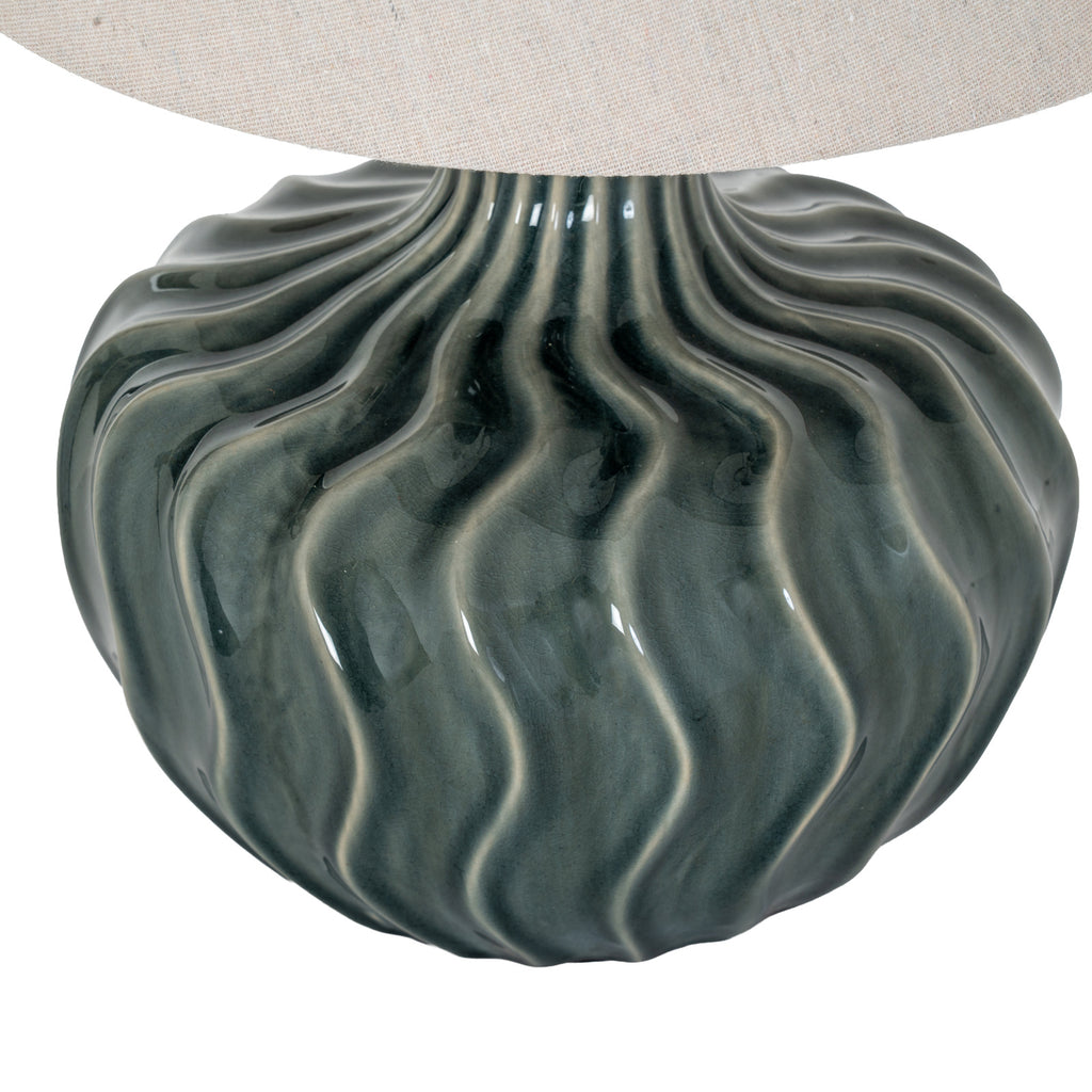 Close-up of the lamp's glossy blue-green curves and lighter flute edges beneath the woven pale shade.