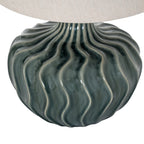 Close-up of the lamp's glossy blue-green curves and lighter flute edges beneath the woven pale shade.