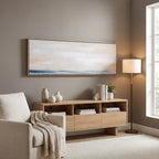 Blush and blue abstract artwork hung above a wooden sideboard on a taupe wall, beside a cream armchair and a floor lamp.