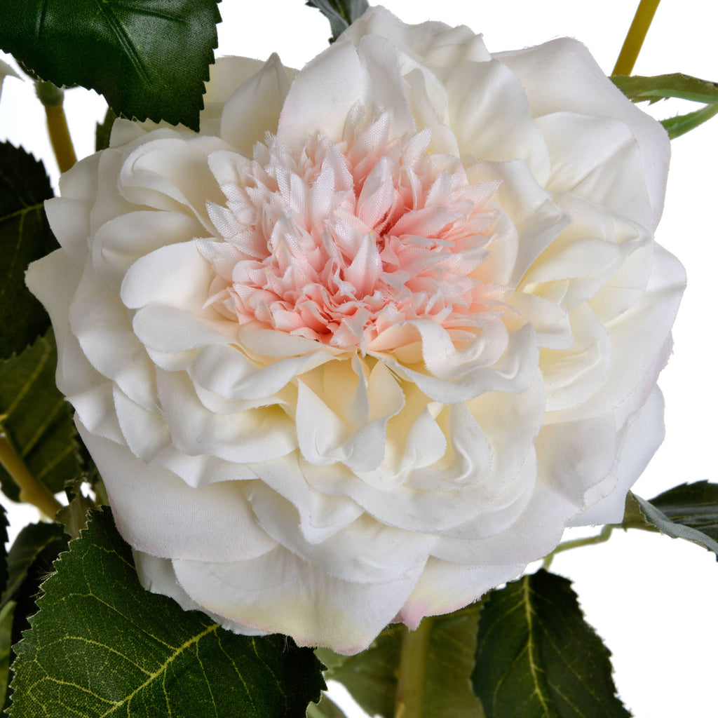 Close-up of the artificial rose's densely ruffled blush-pink centre surrounded by layers of white petals and veined green foliage.