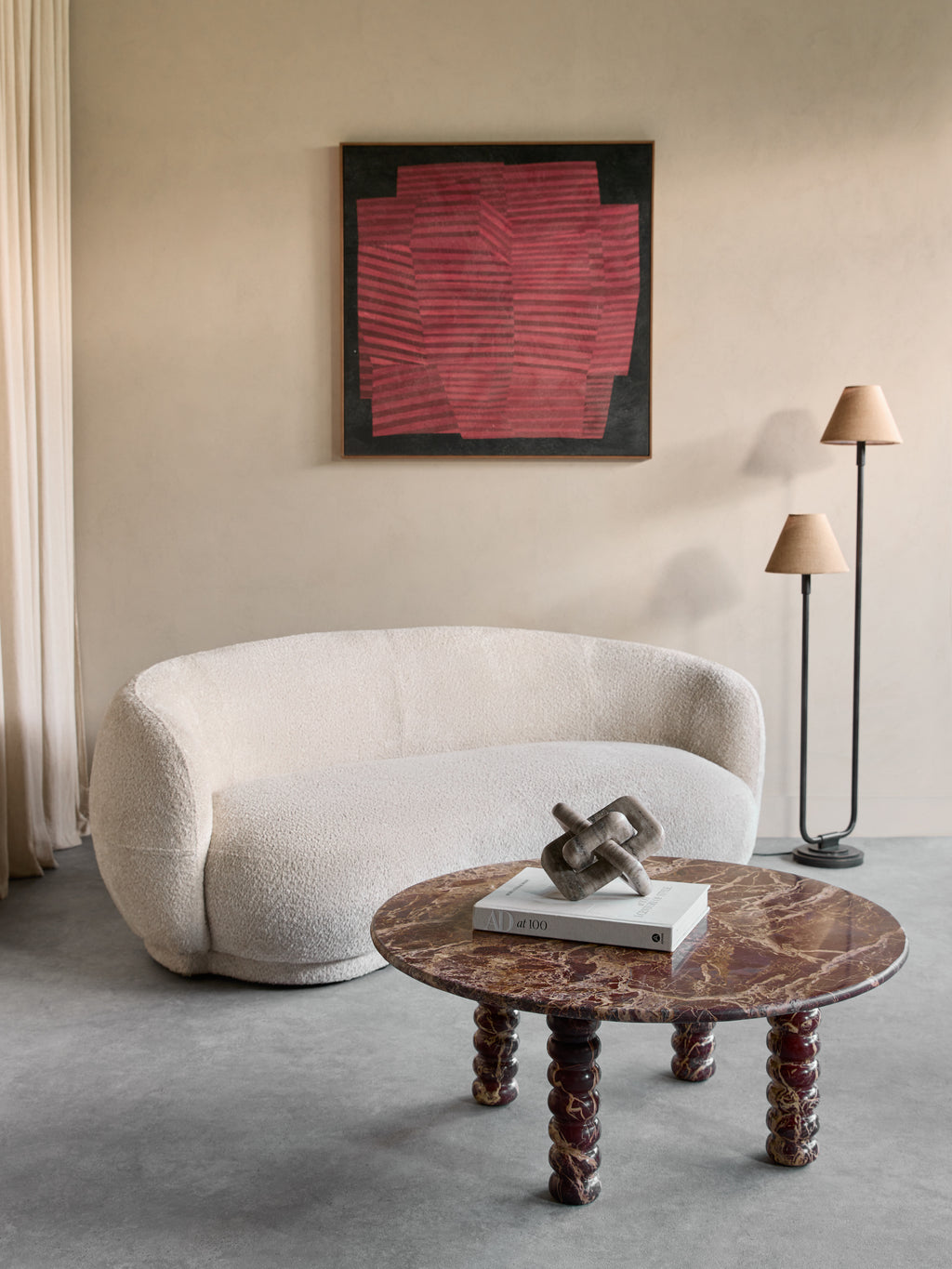 Round burgundy marble coffee table in a seating area with a cream sofa, red abstract artwork and a two-shade floor lamp.