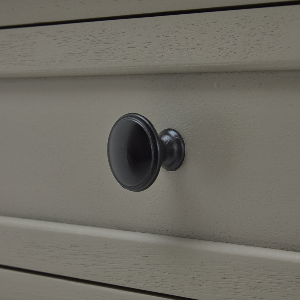 Dark round drawer knob against the pale grey drawer front, with fine surface grain and raised framing visible.
