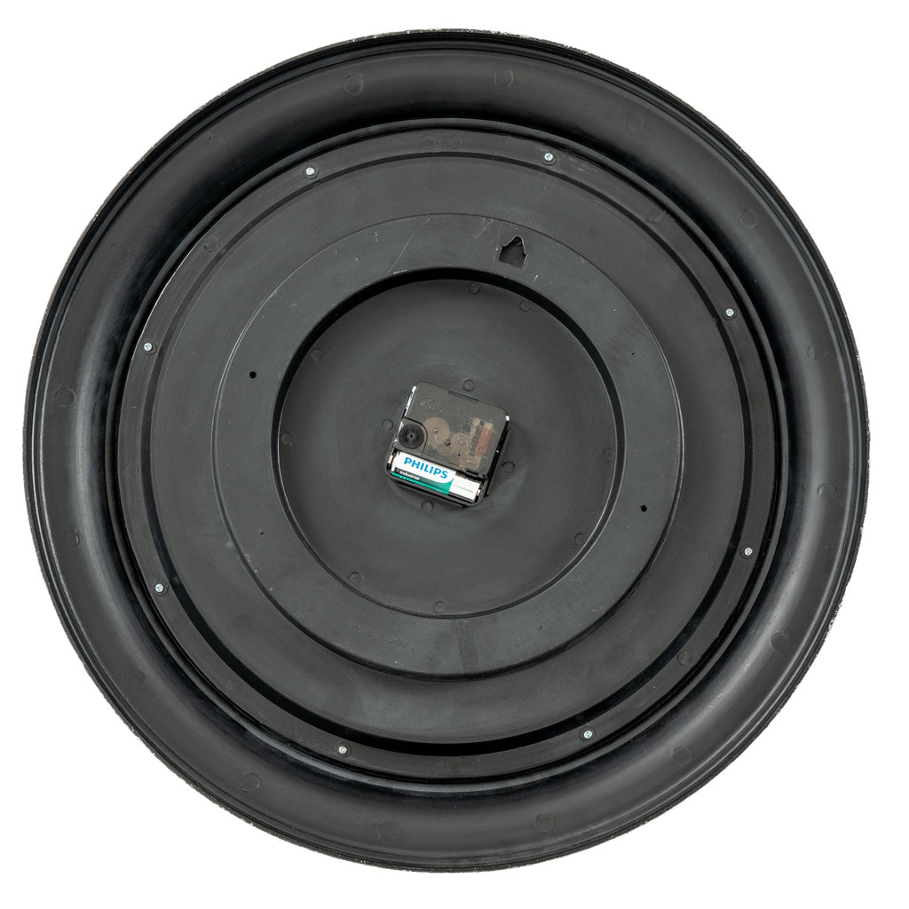 Rear view of the clock showing its circular black back, perimeter screws, hanging aperture and central movement with a battery pictured in place.