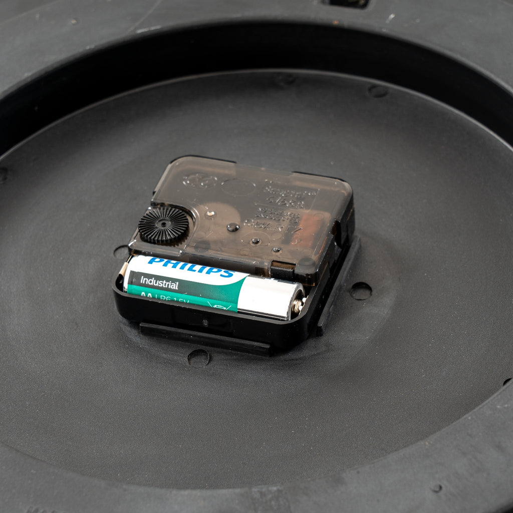 Close-up of the central rear clock movement, with its adjustment wheel and a single battery pictured in the compartment.