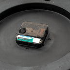 Close-up of the central rear clock movement, with its adjustment wheel and a single battery pictured in the compartment.
