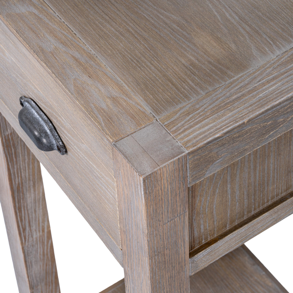 Angled close-up of the tabletop corner, drawer front and side panel with light grain highlights across the pale-brown surface.