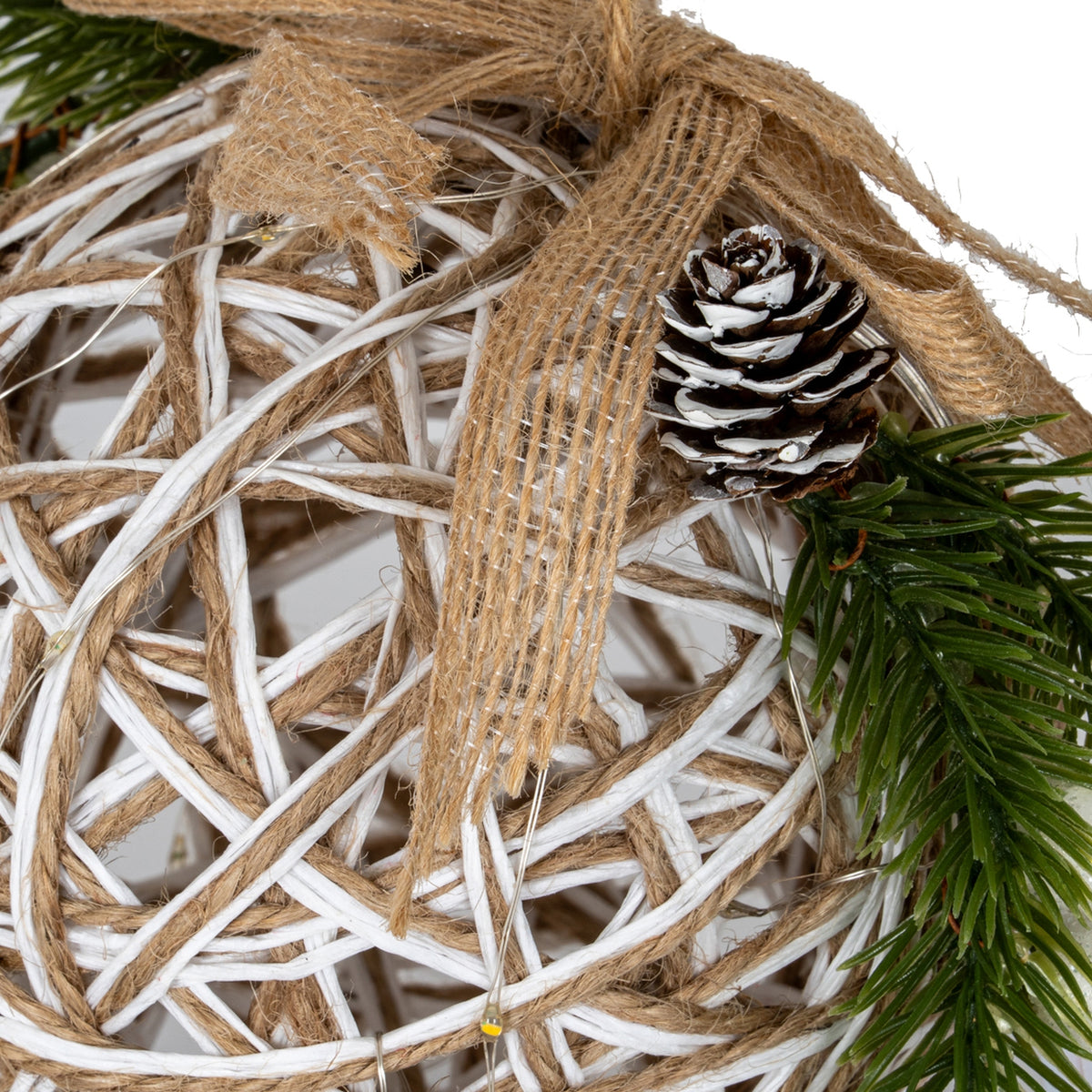 Close-up of the frayed tan bow, white-tipped brown pinecone and green pine spray against the bauble's criss-cross white-and-tan lattice.