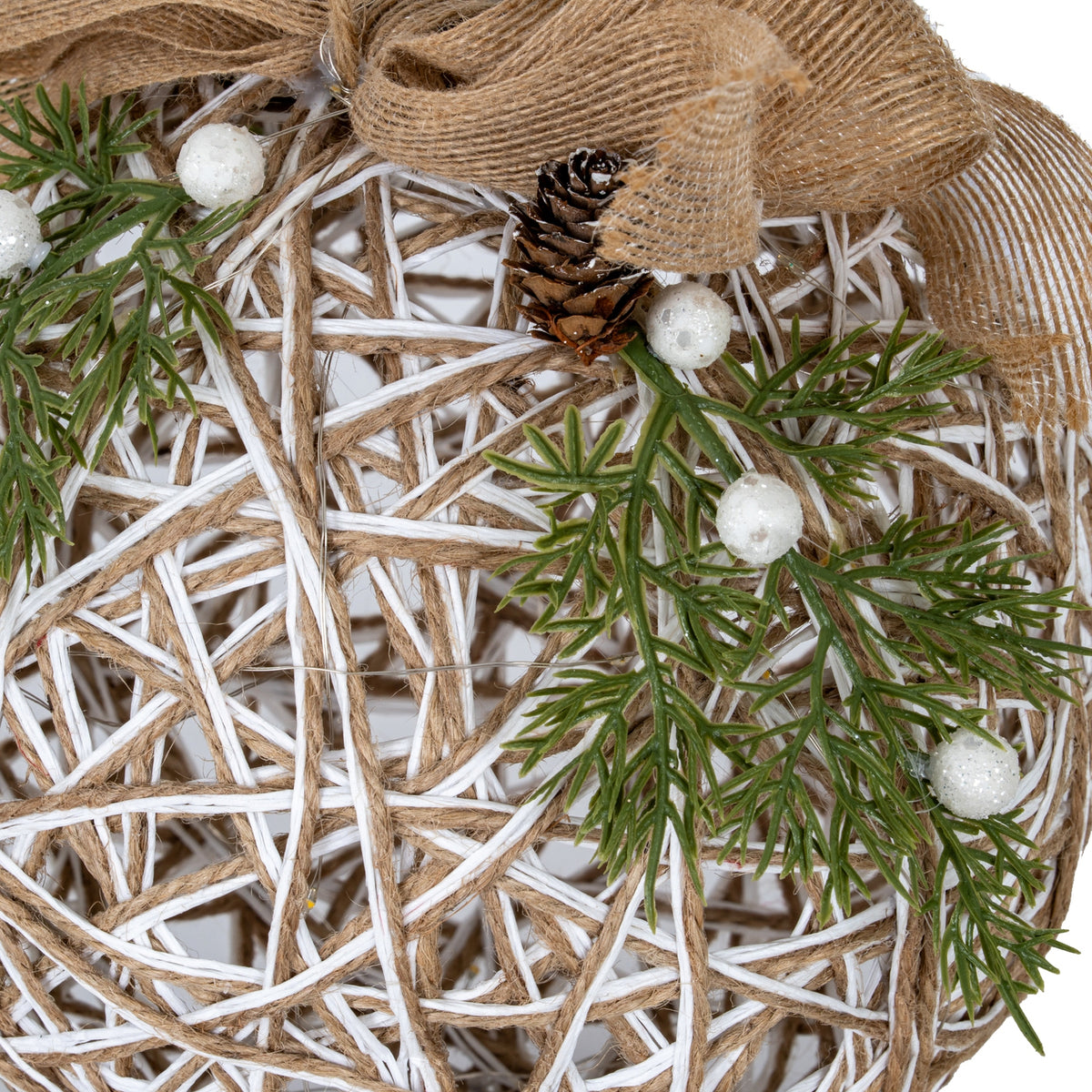 Close-up of the bauble's tan bow and brown pinecone above green branching foliage and glittery white berries, with silver-coloured wire across the open lattice.