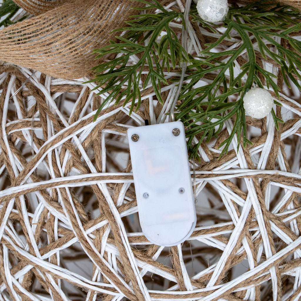Close-up of the attached white battery and control box against the bauble's white-and-tan lattice, beneath green foliage and glittery white berries.