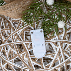 Close-up of the attached white battery and control box against the bauble's white-and-tan lattice, beneath green foliage and glittery white berries.