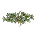 Sage-green artificial foliage bouquet laid horizontally on white, with a tan bow at the centre and tiny white flower or bud details among the leaves.