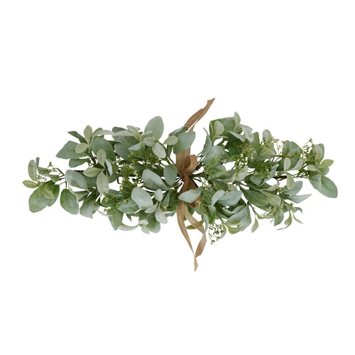 Sage-green artificial foliage bouquet laid horizontally on white, with a tan bow at the centre and tiny white flower or bud details among the leaves.